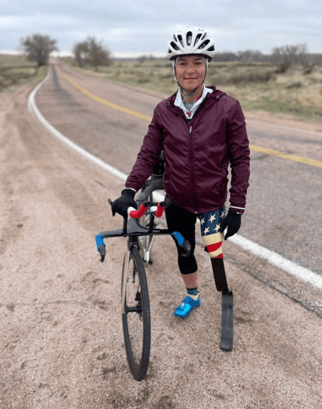 Women bicyclist on the side of the road standing next to bike. 