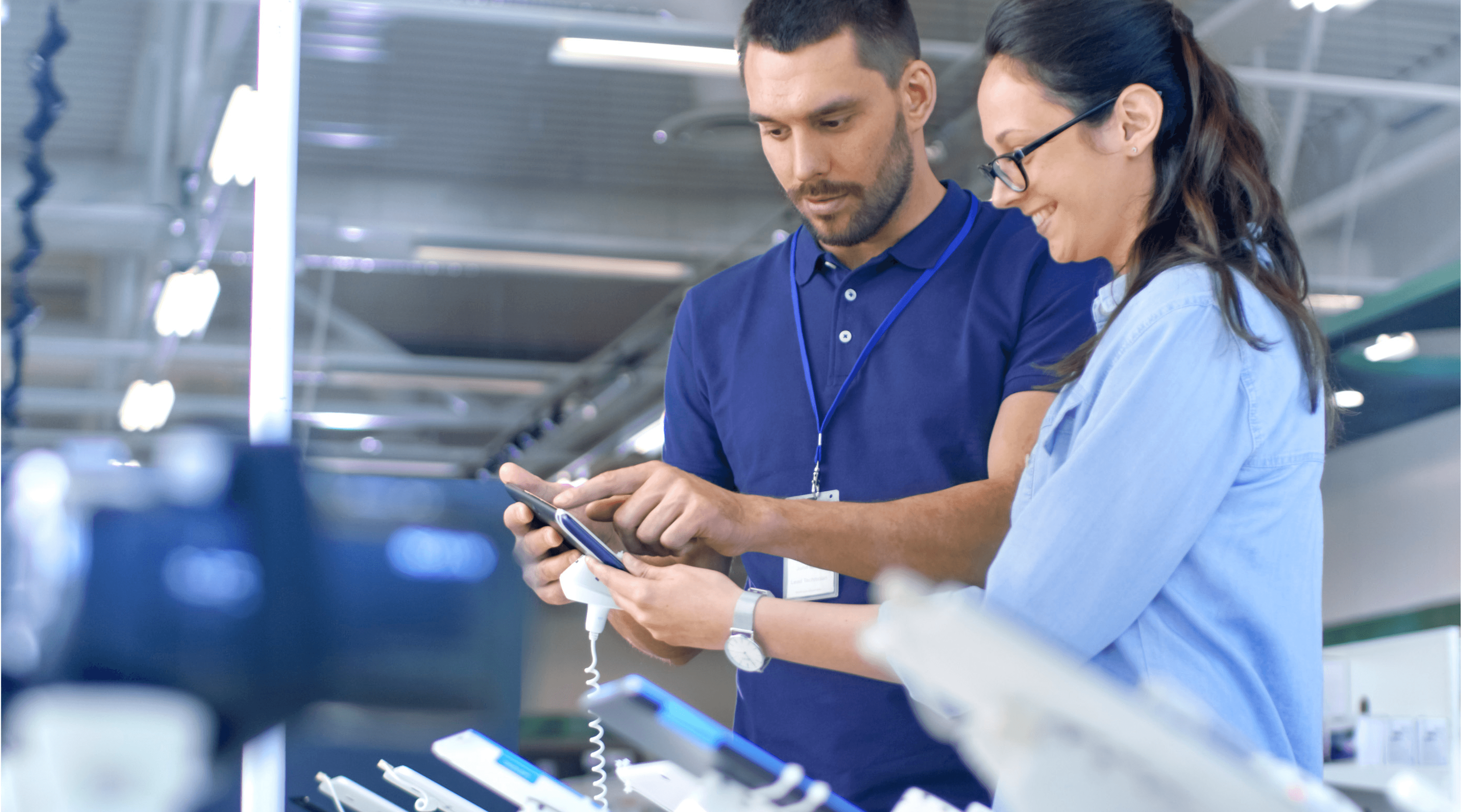 Man and women standing over multiple tablets using a mobile device.